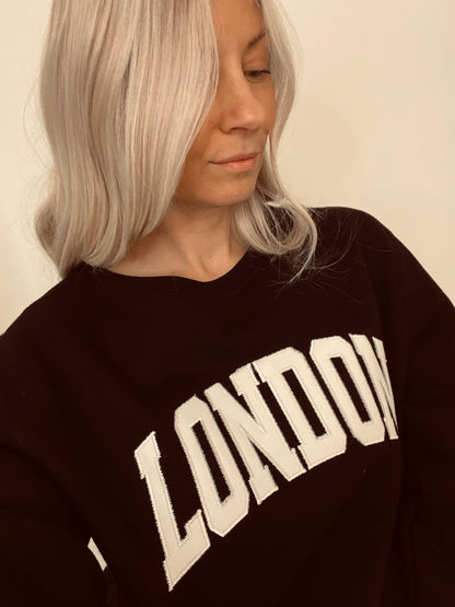 women wearing a black crewneck with 'LONDON' embroidered on it.